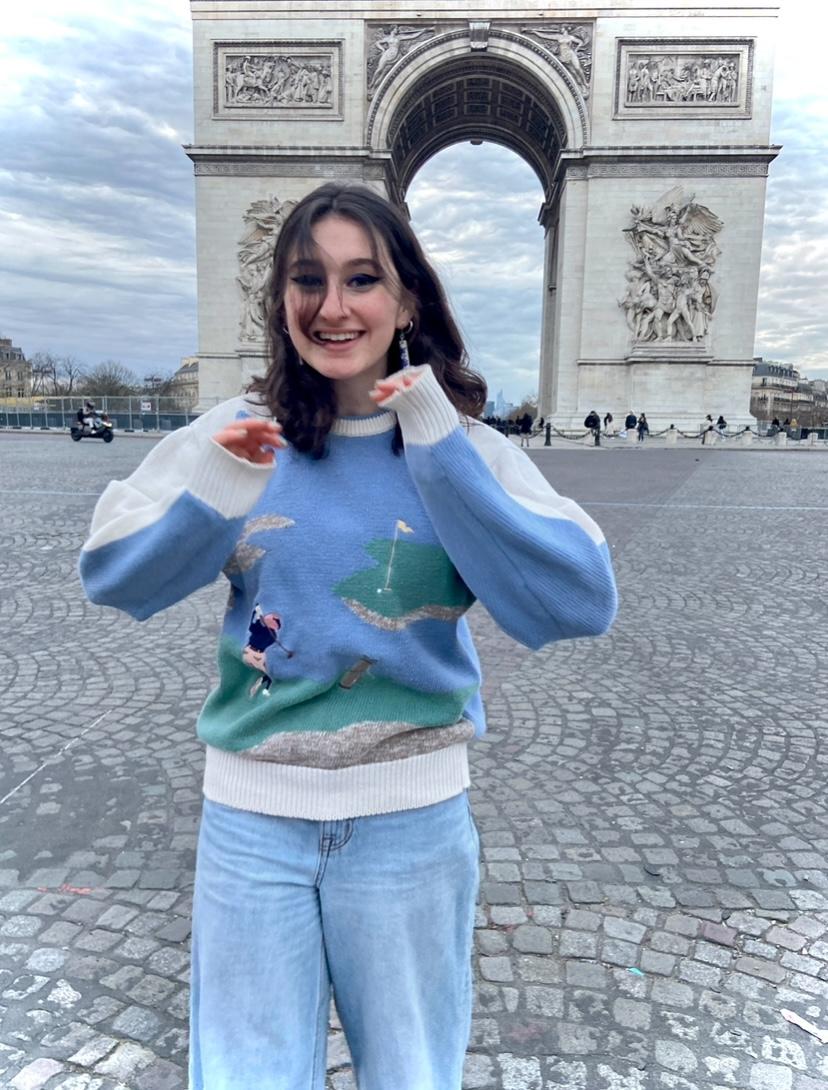 Chloe Brookes in a blue sweater and dark hair posing in front of the Arc de Triomphe