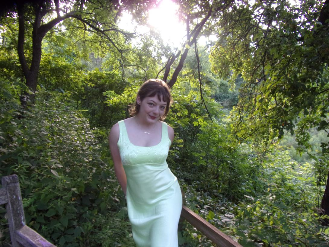 Helena is a woman with short dark hair in a green dress posing an a forest